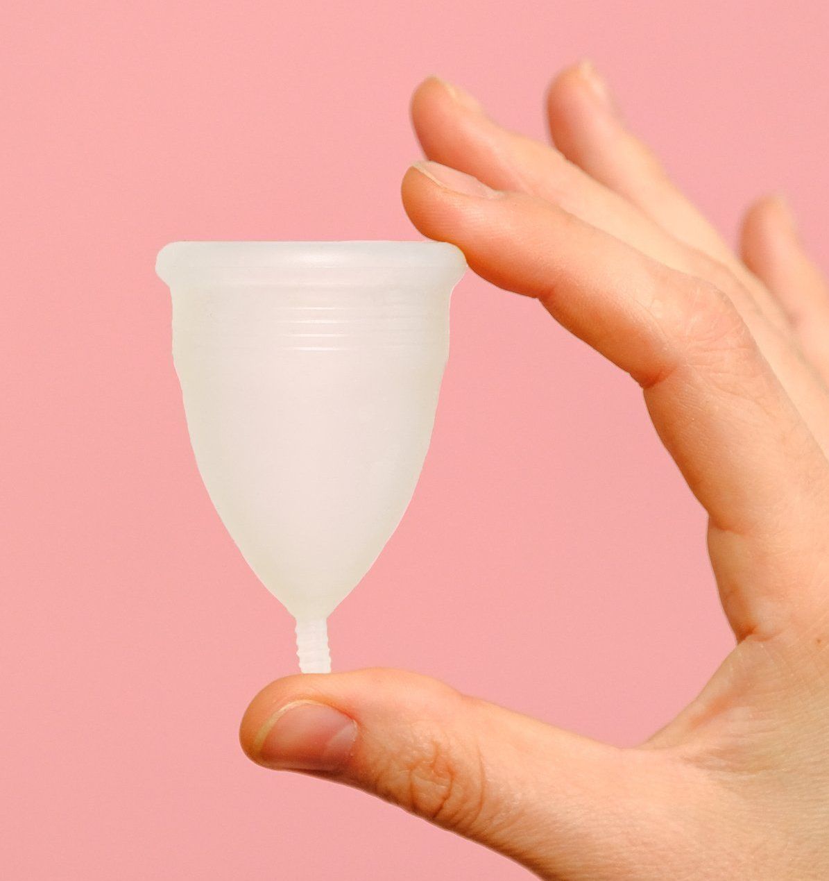 Hand holding a white menstrual cup, pink background.