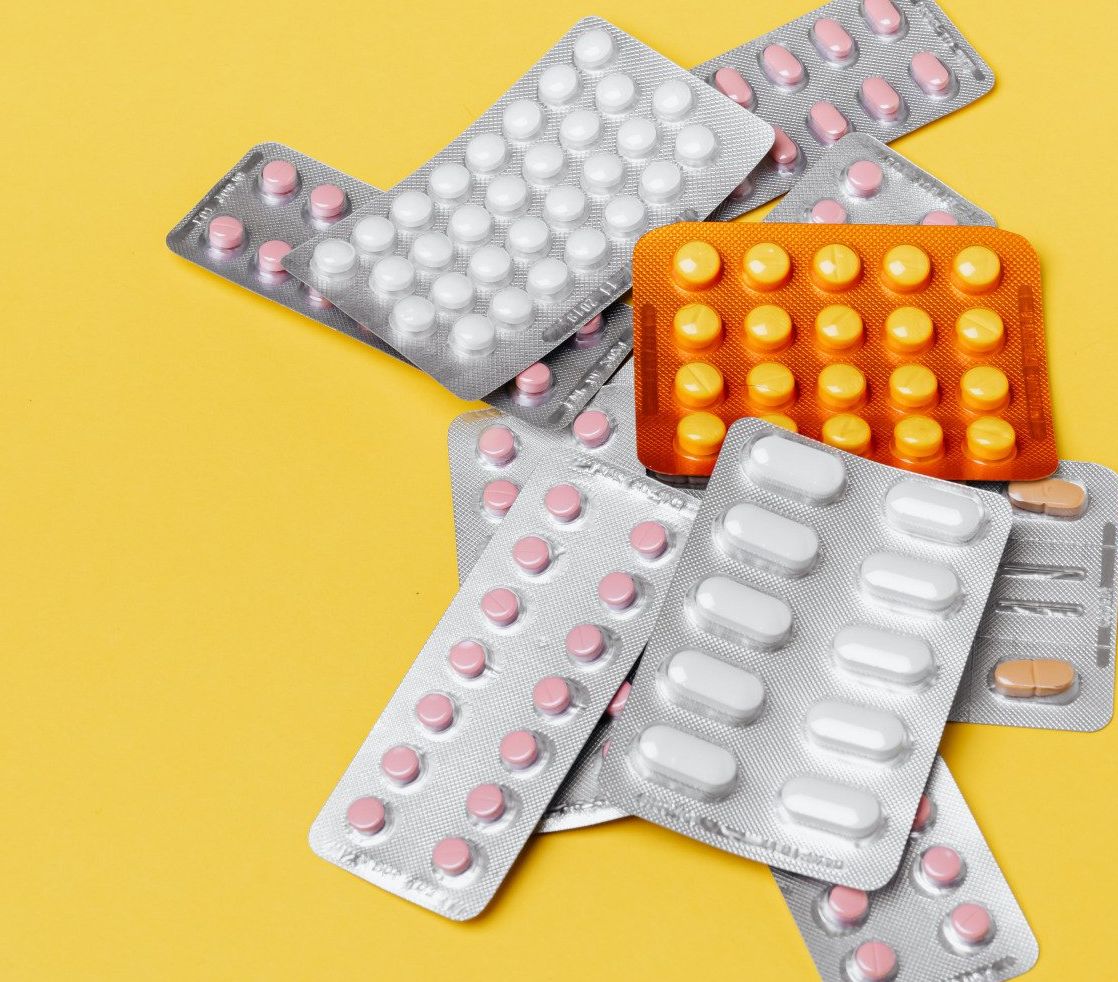 Blister packs of pills in various colors on a yellow background.