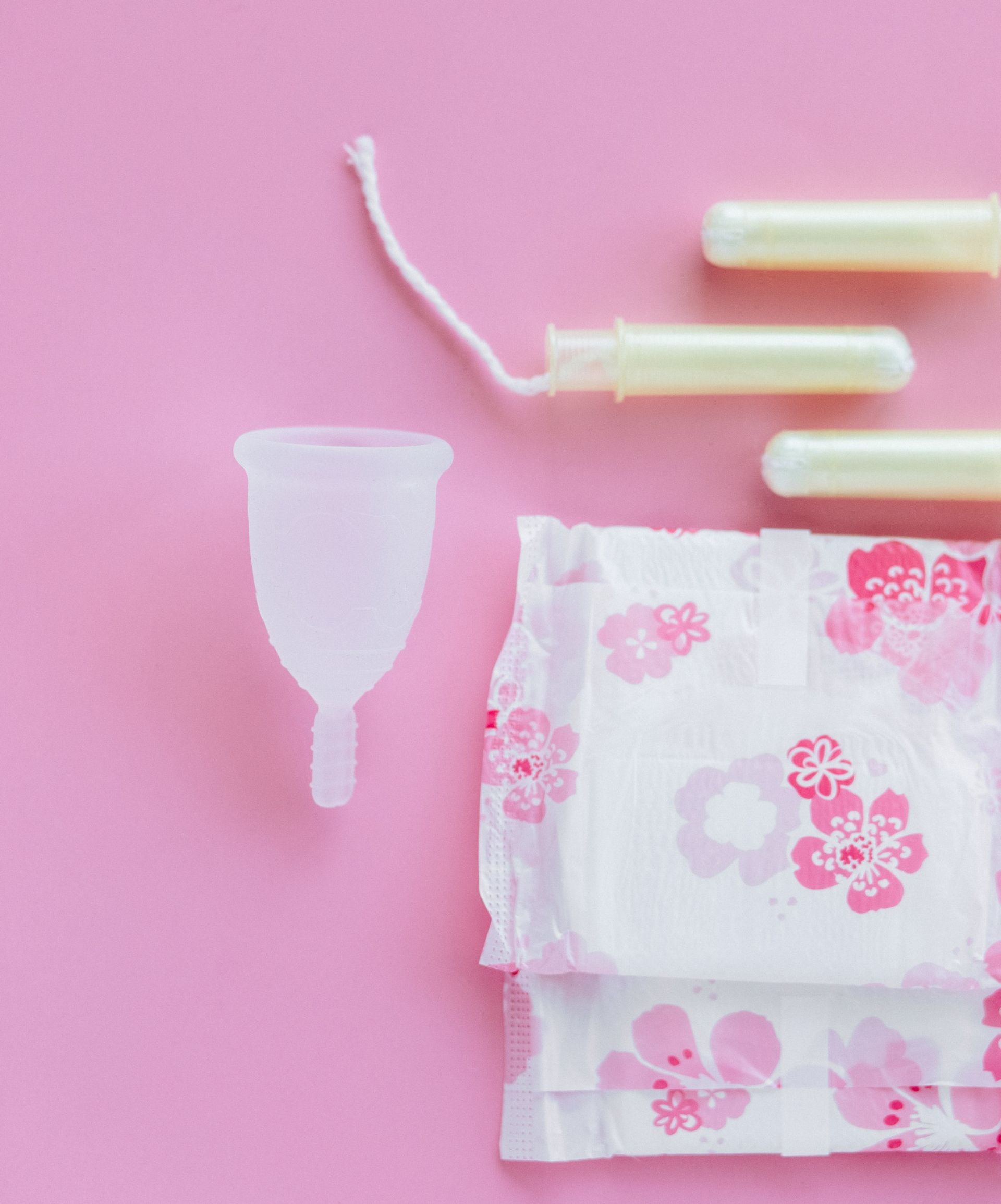 Menstrual cup, tampons, and pads on a pink background.