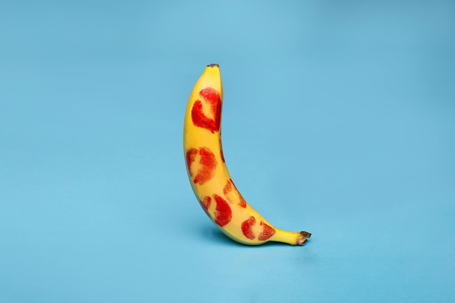 Banana with red lipstick kisses on a blue background.