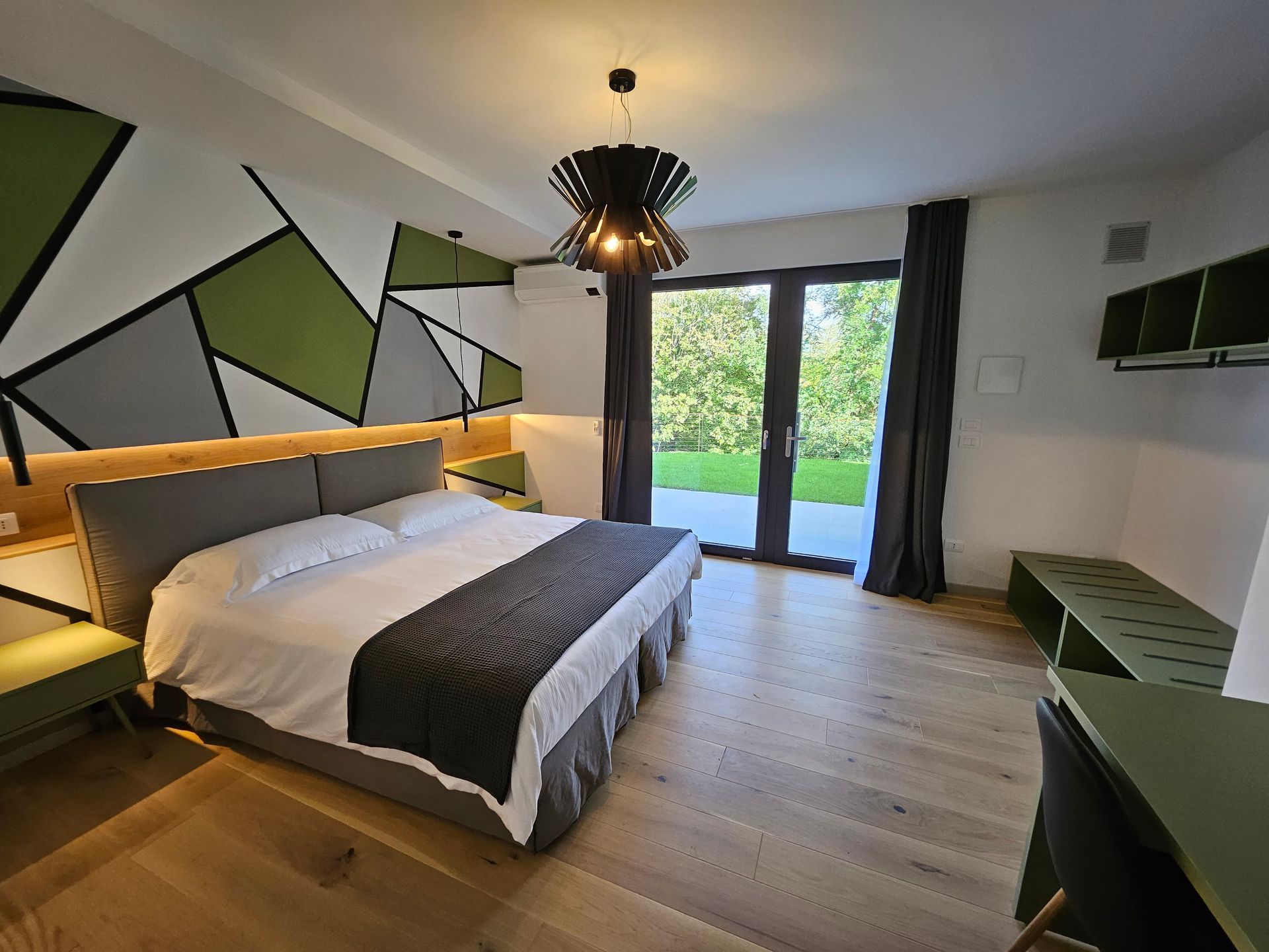 Camera d'albergo moderna con decorazioni murali geometriche, letto king size e porte finestre che si affacciano sul giardino.