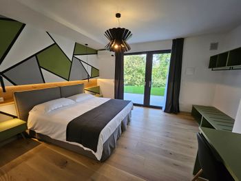 Camera d'albergo moderna con letto king size, decorazioni murali geometriche, scrivania e porte finestre che si affacciano sul verde.