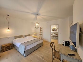 Camera da letto luminosa con letto, scrivania, sedia, TV a parete e luci a sospensione soffuse.
