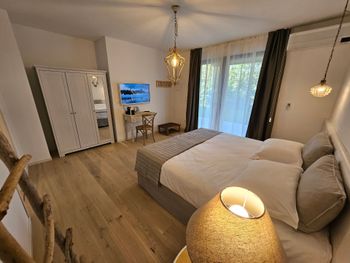 Luminosa camera da letto moderna con letto, TV, scrivania, pavimento in legno e ampie tende alle finestre.