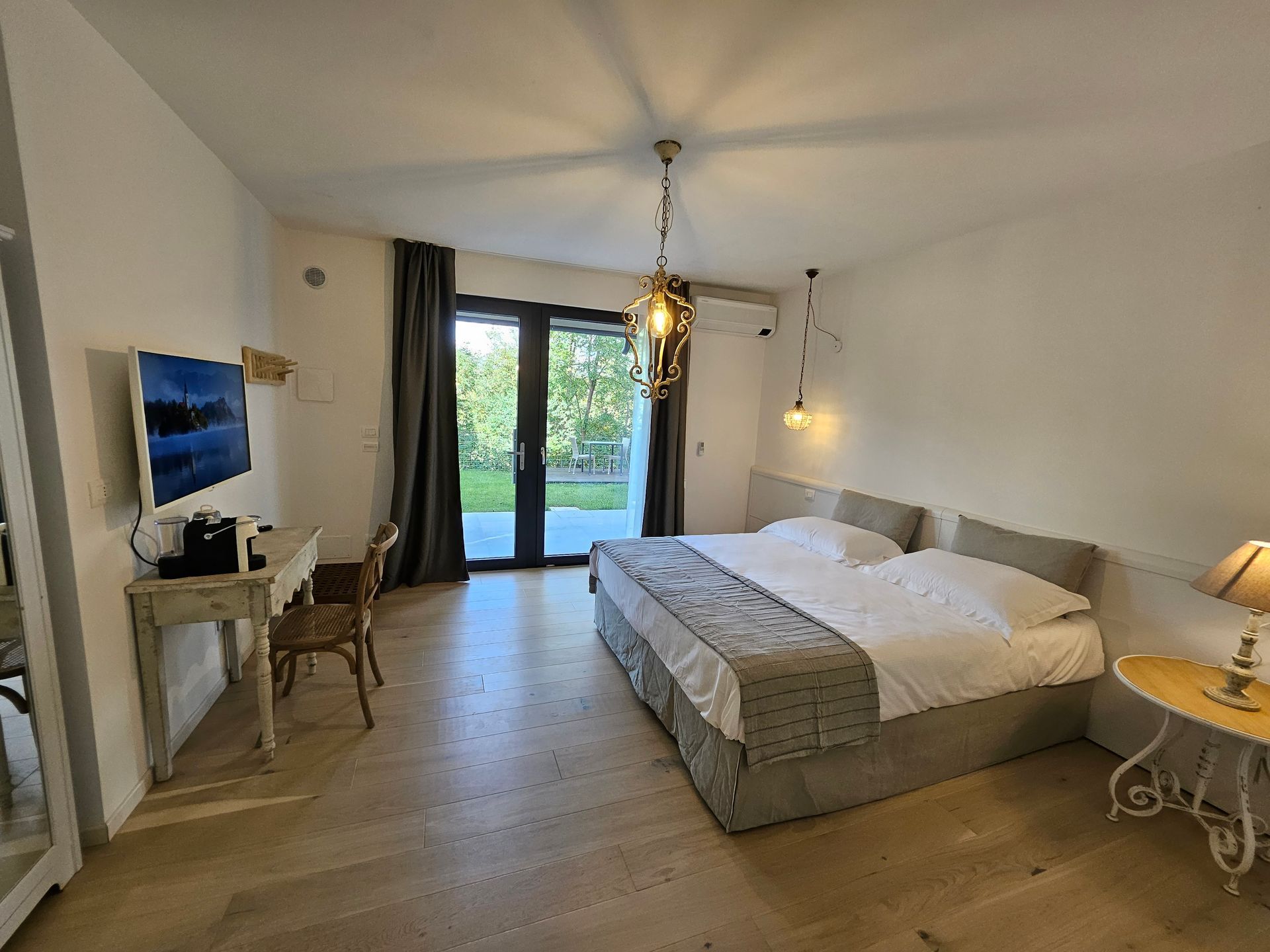 Camera da letto luminosa con un grande letto, scrivania, lampada e porte finestre che si aprono su un patio.