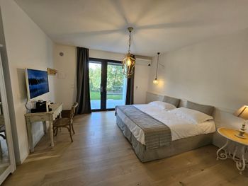 Camera da letto luminosa con un grande letto, scrivania, lampada e porte finestre che si aprono su un patio.