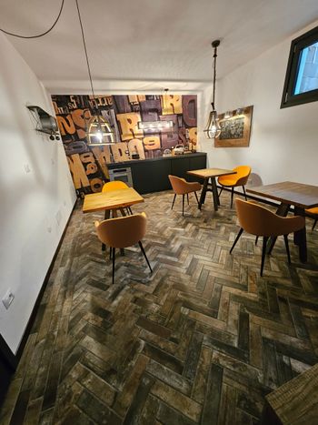 Piccolo caffè con tavoli e sedie in legno, pavimento decorato, decorazioni alle pareti e un'accogliente area salotto.