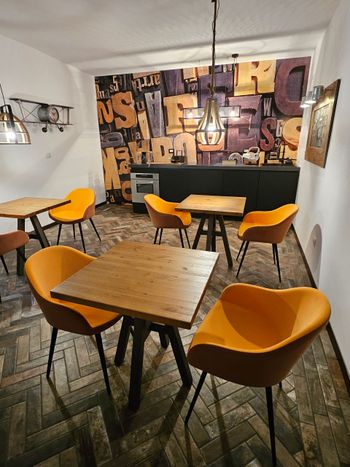 Interno vuoto di un caffè con tavoli in legno, sedie color senape, lampade a sospensione e decorazioni murali con graffiti.