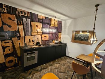 Cucina moderna con mobili neri, quadri in legno decorati alle pareti e una lampada a sospensione sopra un tavolino.