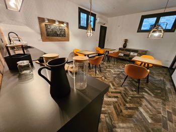 Interno moderno di un caffè con bancone nero, tavolini rotondi, sedie arancioni e pavimento piastrellato con motivi decorativi.