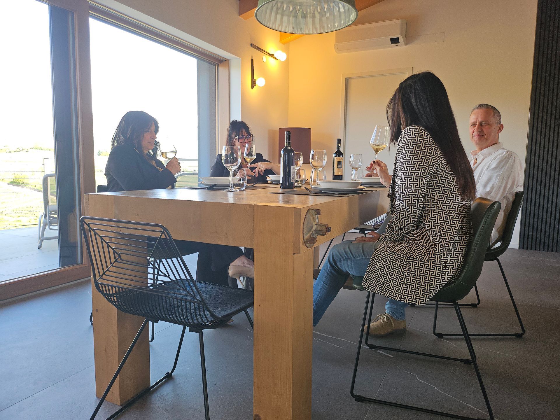 In una stanza luminosa, alcune persone erano sedute attorno a un tavolo di legno e conversavano vicino a una grande porta aperta.