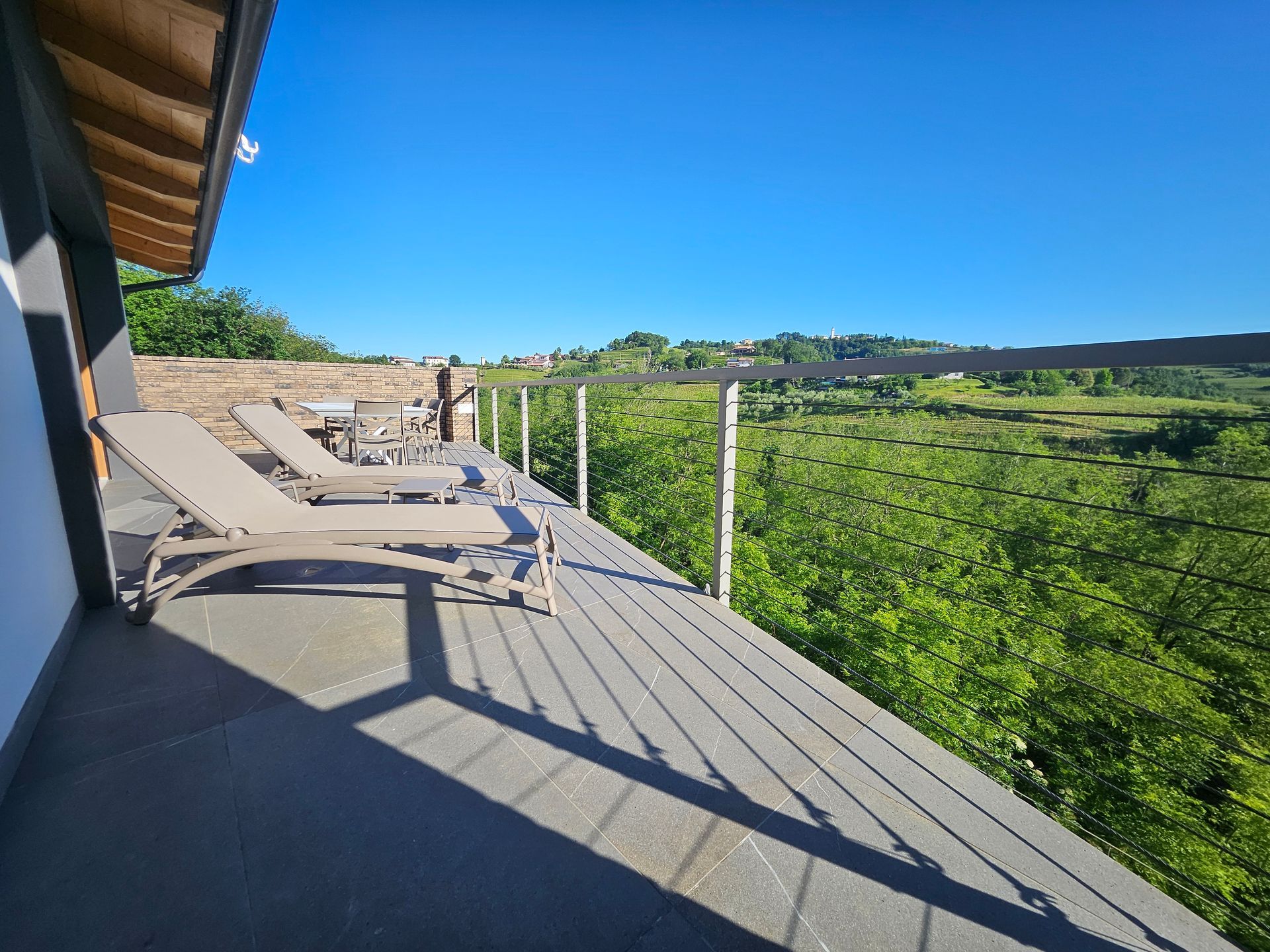 Patio soleggiato con sedie a sdraio che si affaccia su una verde collina e sul cielo azzurro.
