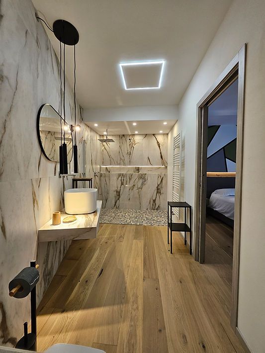 Stretto corridoio moderno con pavimento in legno, pareti in marmo, luci a LED a soffitto e porta aperta che conduce a una camera da letto.