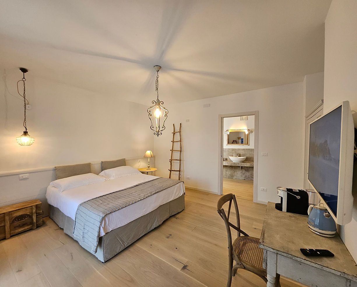 Camera da letto luminosa con letto, scrivania, lampade a sospensione e porta che conduce al bagno.