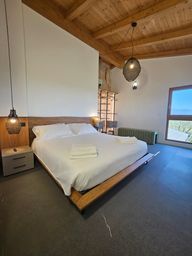 Camera da letto moderna con letto bianco, dettagli in legno, lampade a sospensione e ampia finestra con vista sull'oceano.