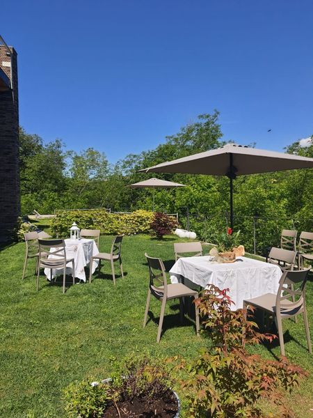 Tavolini da caffè all'aperto con tovaglie bianche e grandi ombrelloni su un prato verde e soleggiato.