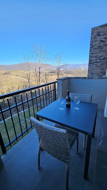 Tavolo e sedie da balcone con vista su una collina soleggiata e un cielo azzurro.