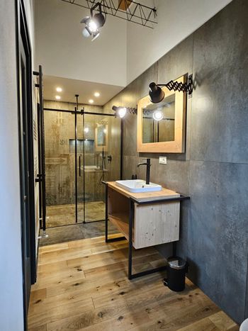 Bagno moderno con doccia in vetro, mobile lavabo in legno, specchio e pareti grigie con finitura materica.