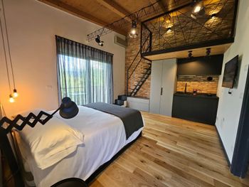 Camera da letto mansardata moderna con letto, mattoni a vista, scala e pavimento in legno.