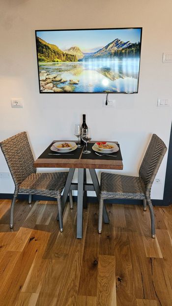 Accogliente angolo pranzo con due sedie decorate, un tavolino per due e un quadro paesaggistico alla parete.