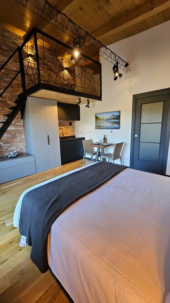 Accogliente camera da letto con letto, ringhiera in legno per il soppalco, quadri alle pareti e porta grigia.