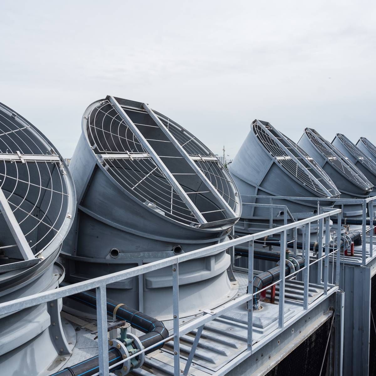 Cooling towers on a rooftop, gray metal structures with protective grates, against a cloudy sky.