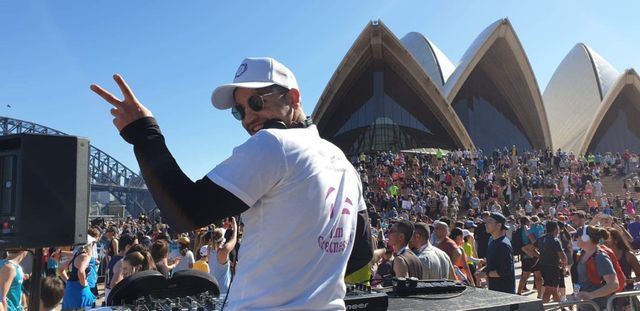 DJ performing outdoors beside Sydney Opera House, with guests in the background.