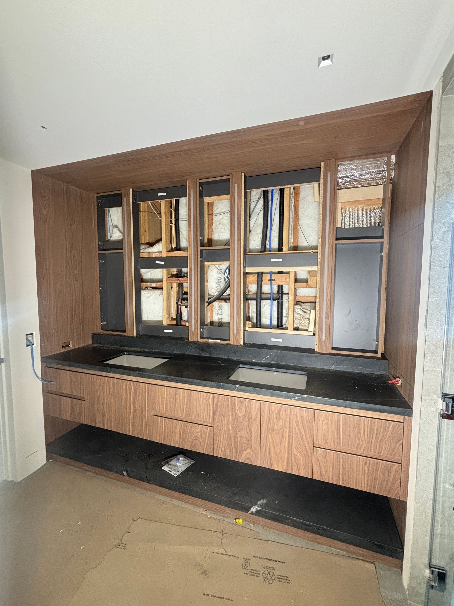 Built-in wood cabinet with glass doors and shelves, black countertop, in a modern room.