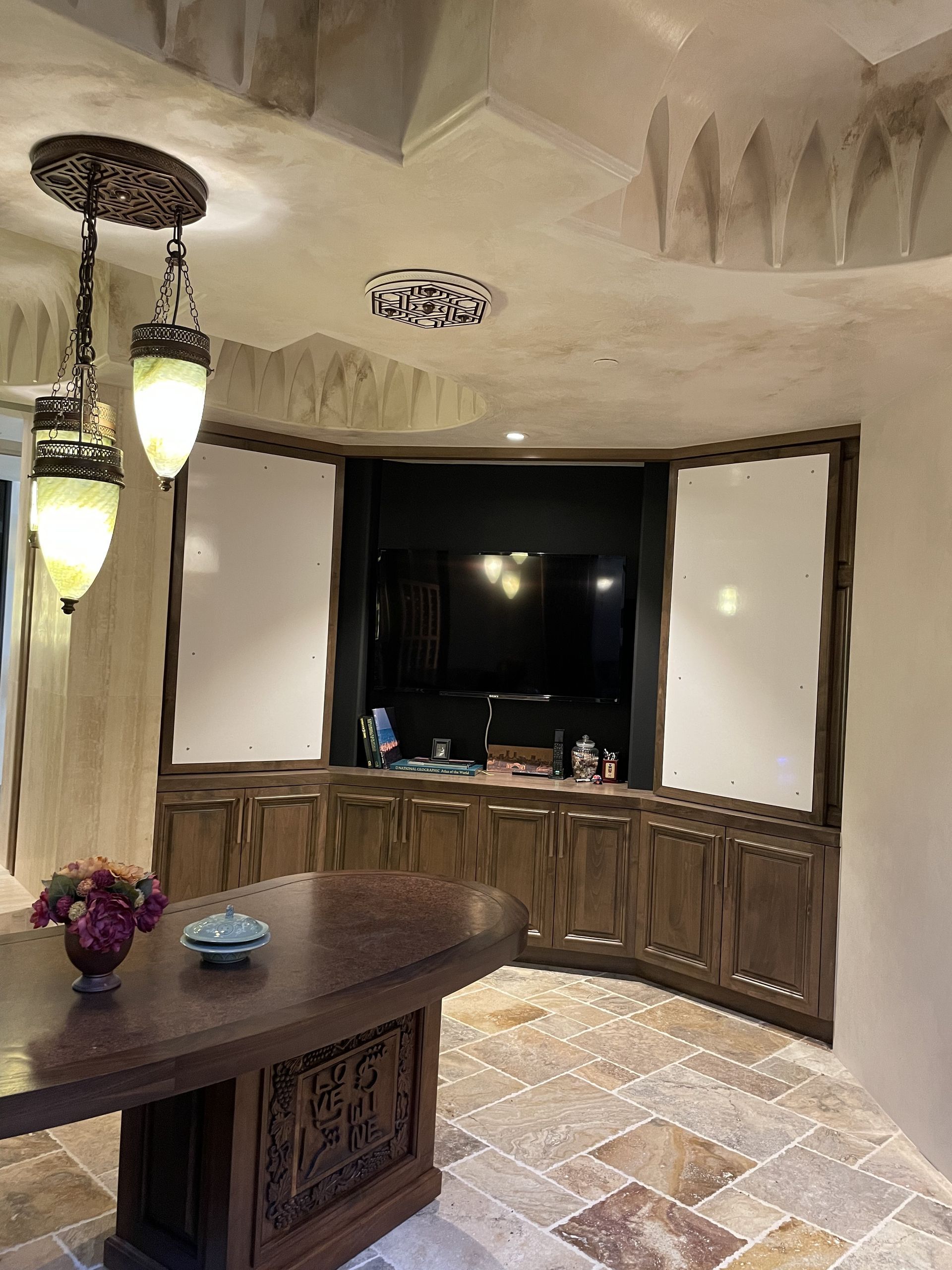 Elegant dining room with curved wood cabinets, stone floor, and a round wooden table near a large window.
