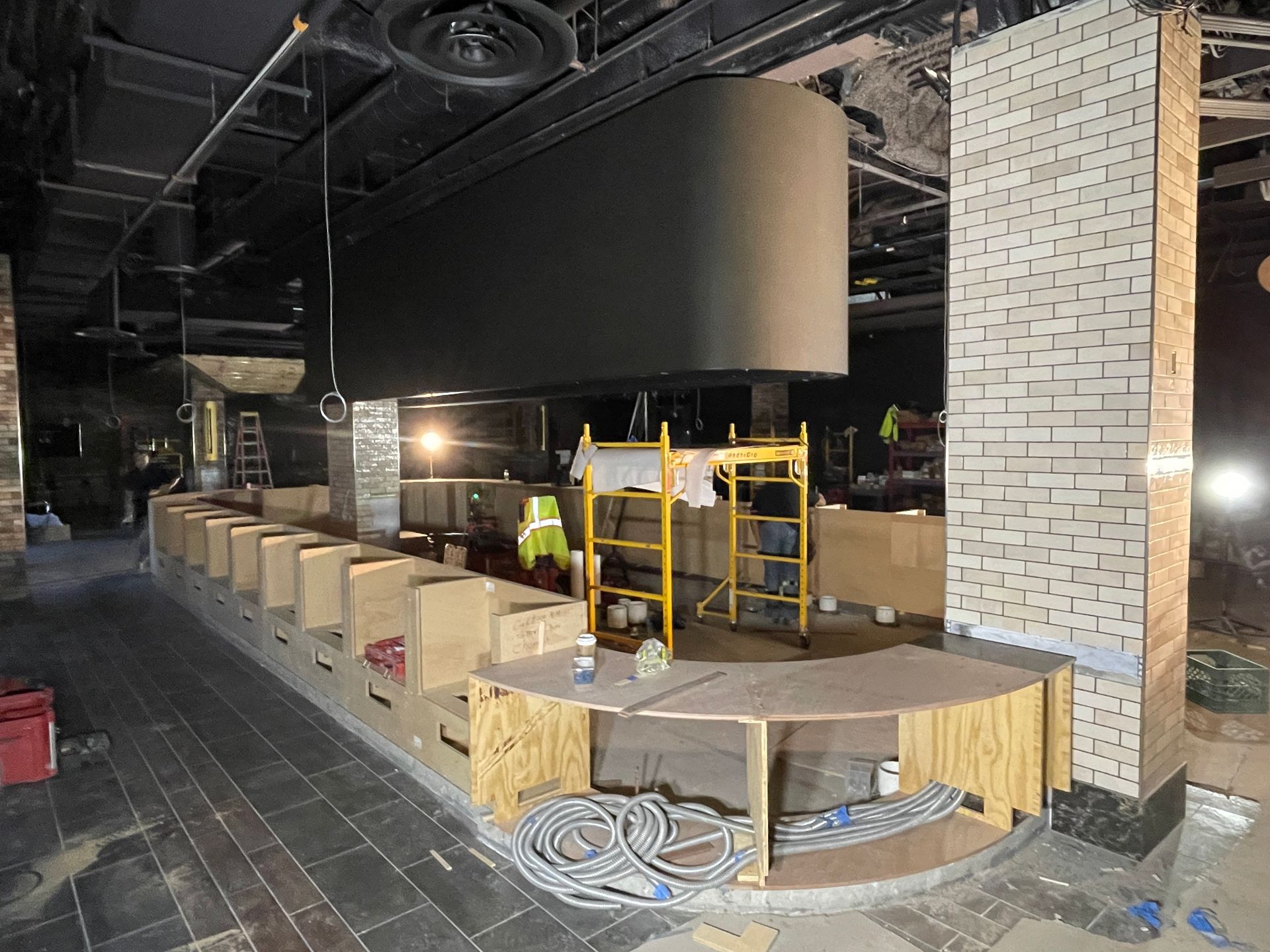 Empty bar interior with tiled floor, wood counters, and a yellow scaffold near a brick column