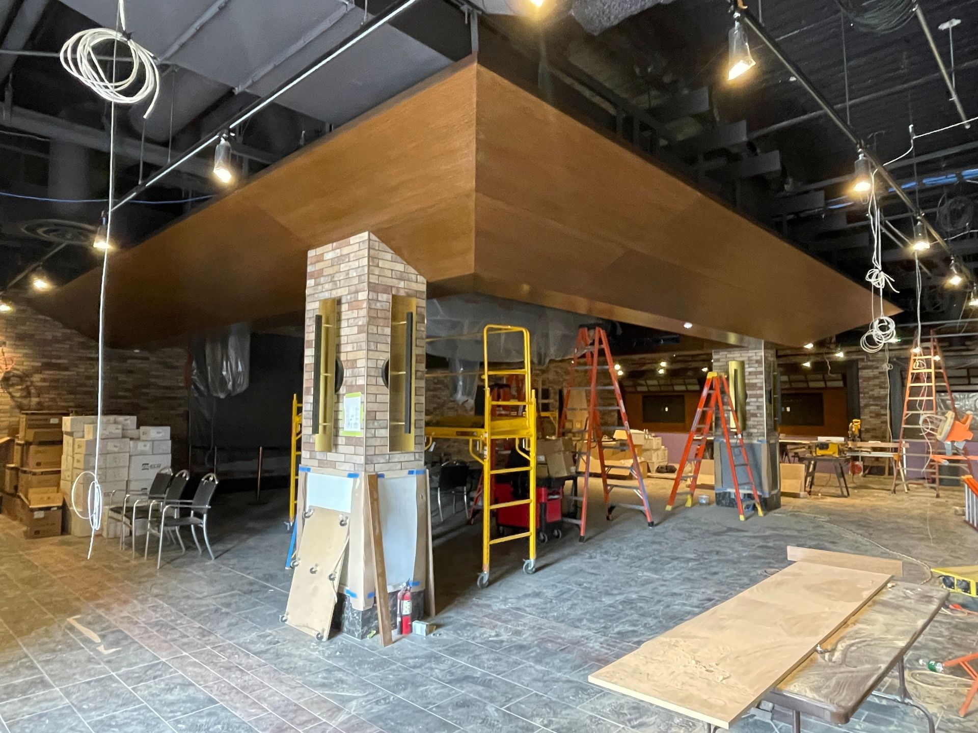 Interior under renovation with ladders, tools, and plywood flooring in a partially finished room