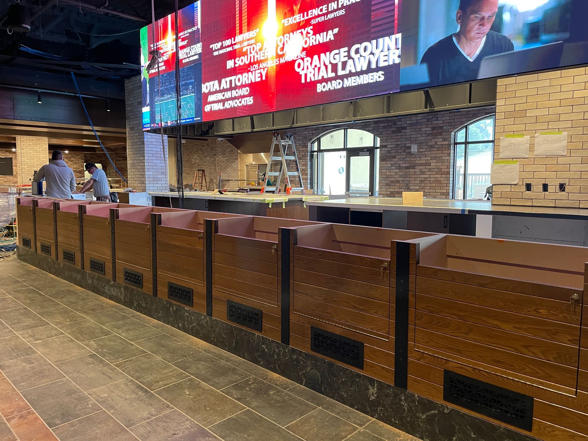 Empty restaurant counter with brown stools and a large illuminated menu board behind it.