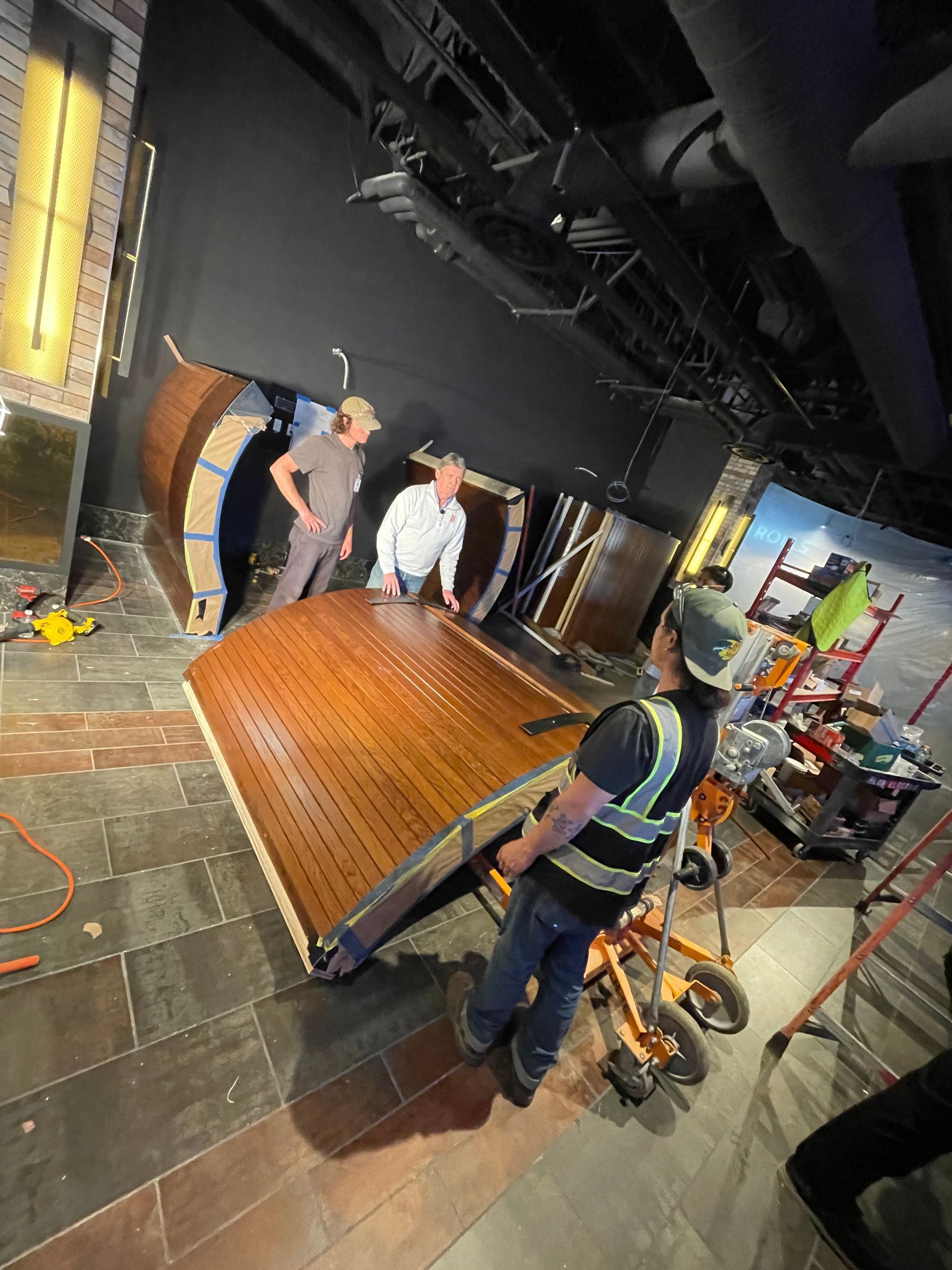 Crew moving a large curved wooden panel in a dark theater backstage area