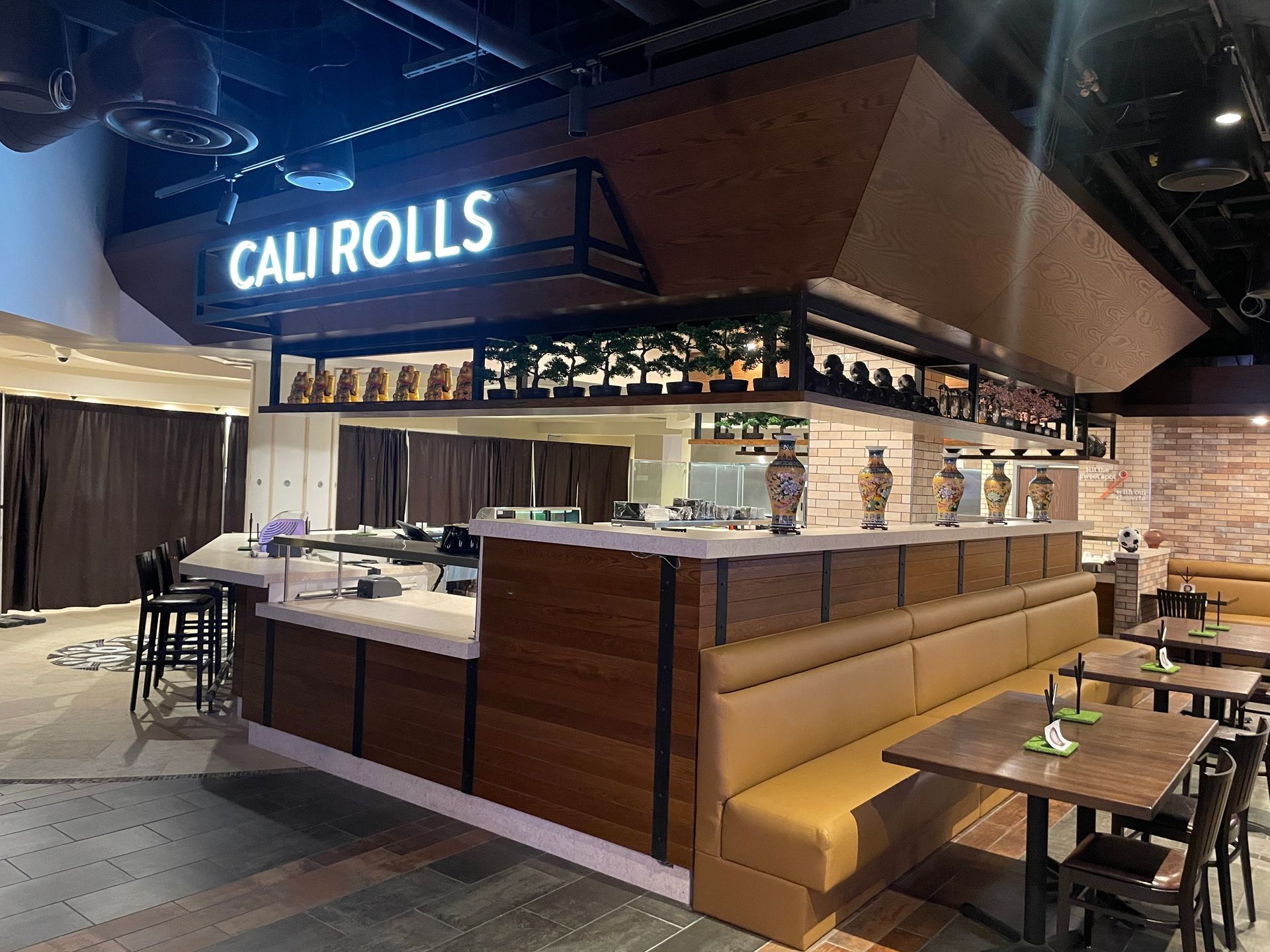 Cali Rolls sushi counter with neon sign, wood booths, and tables in a modern restaurant interior