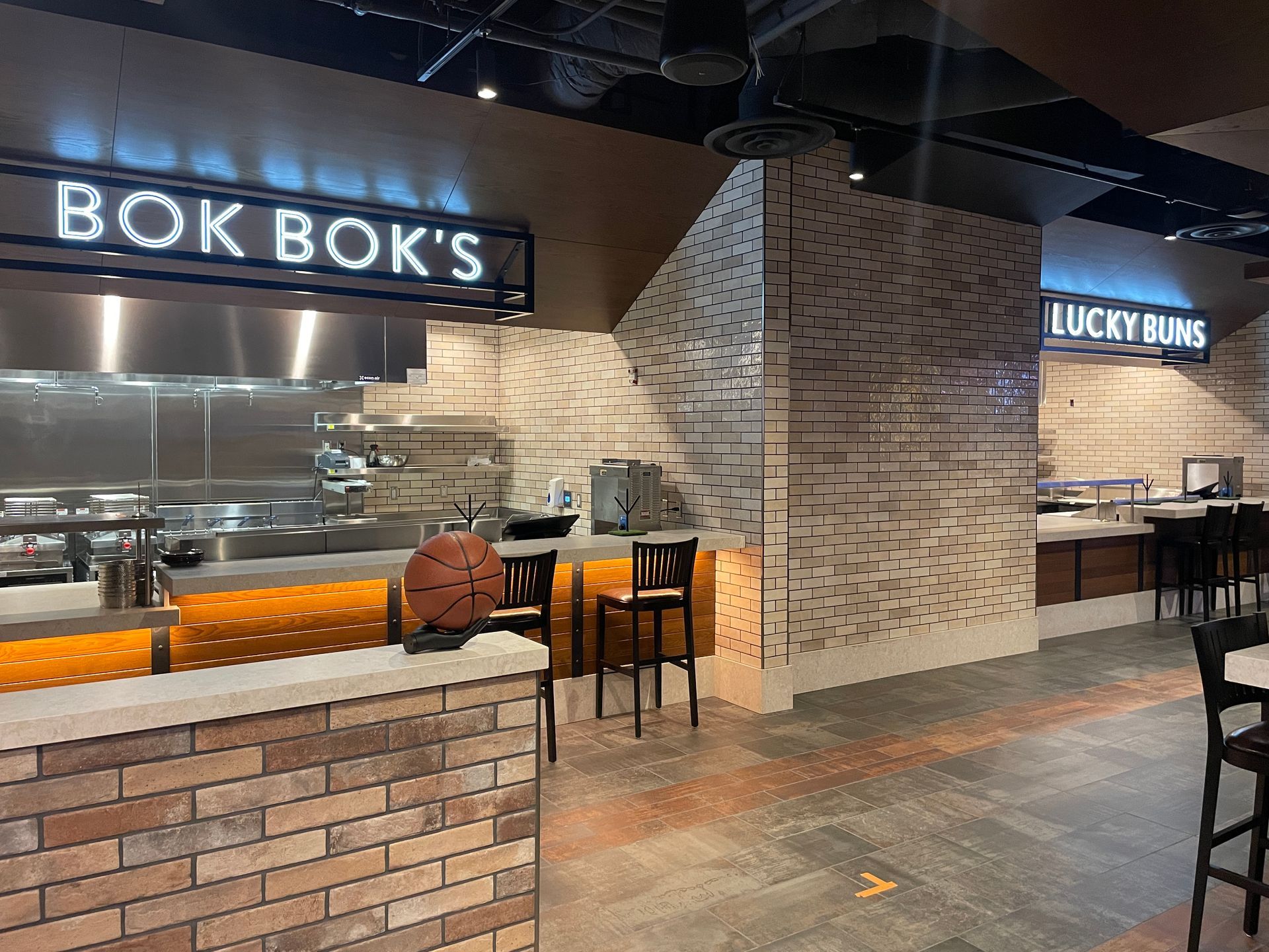 Restaurant food counter with Bok Bok’s and Lucky Buns signs in a brick-lined indoor food hall