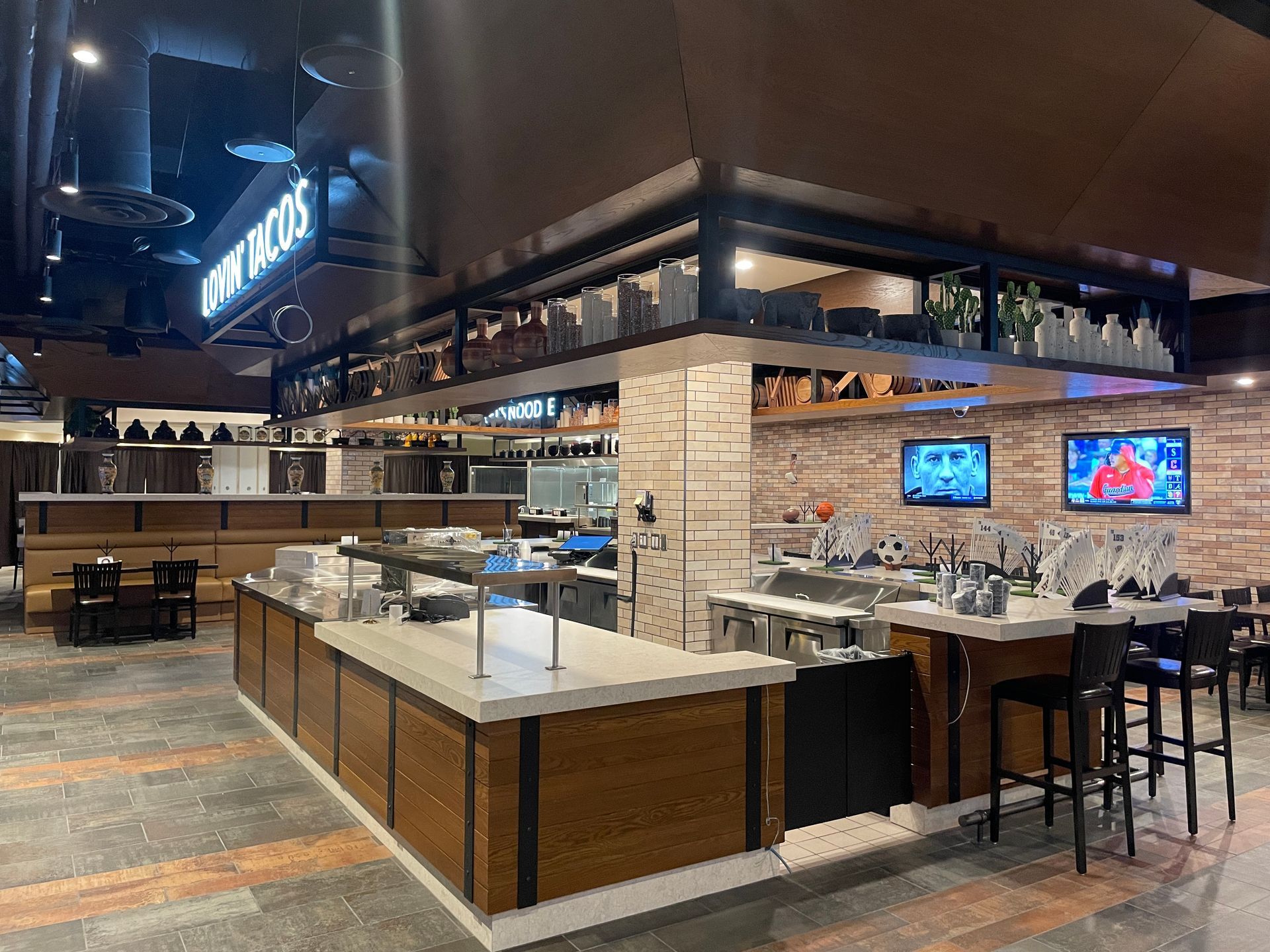 Empty modern restaurant and bar interior with wooden counters, high stools, and wall-mounted TVs