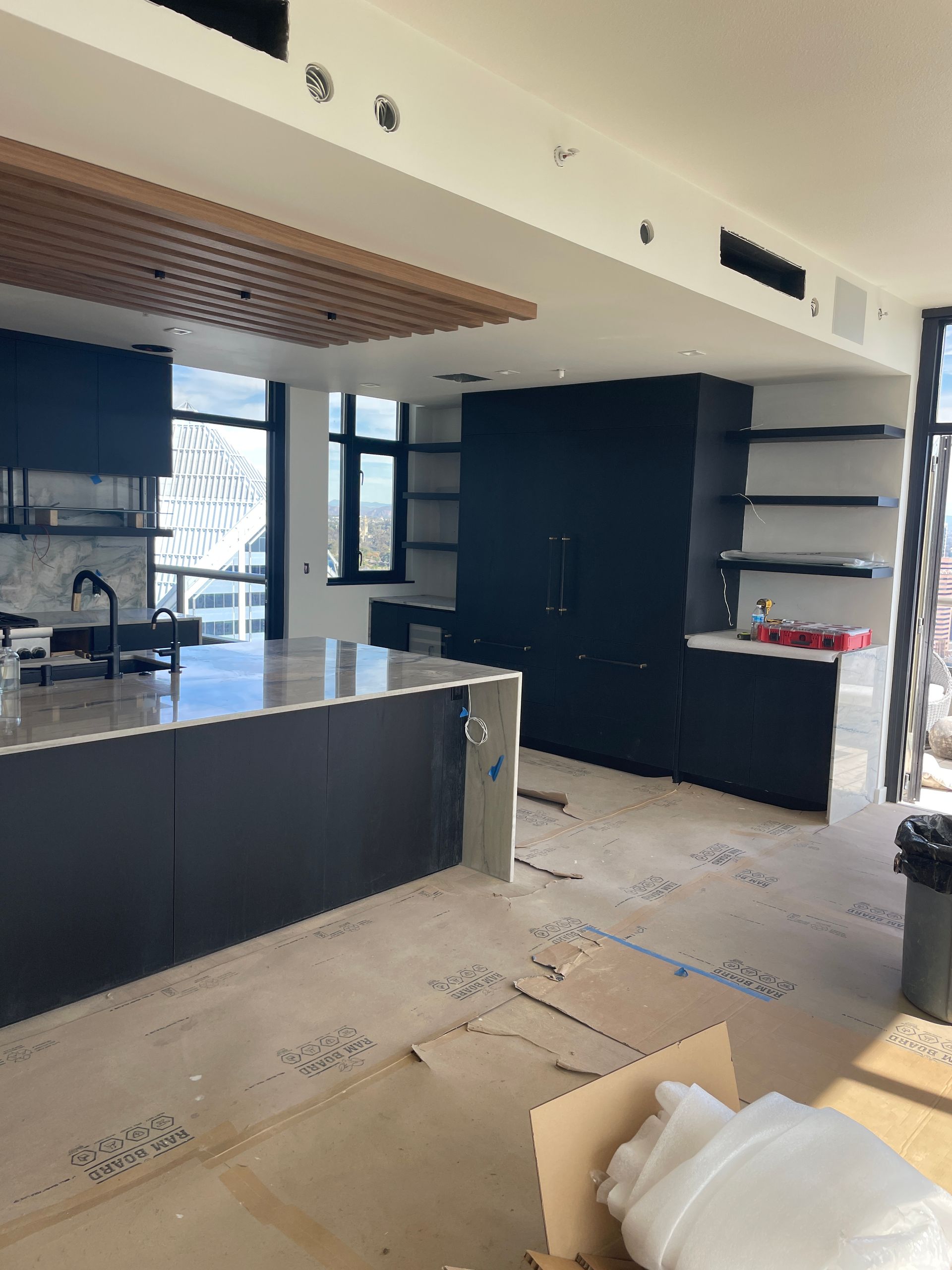 Modern kitchen under renovation with dark cabinets, black countertops, and cardboard on the floor
