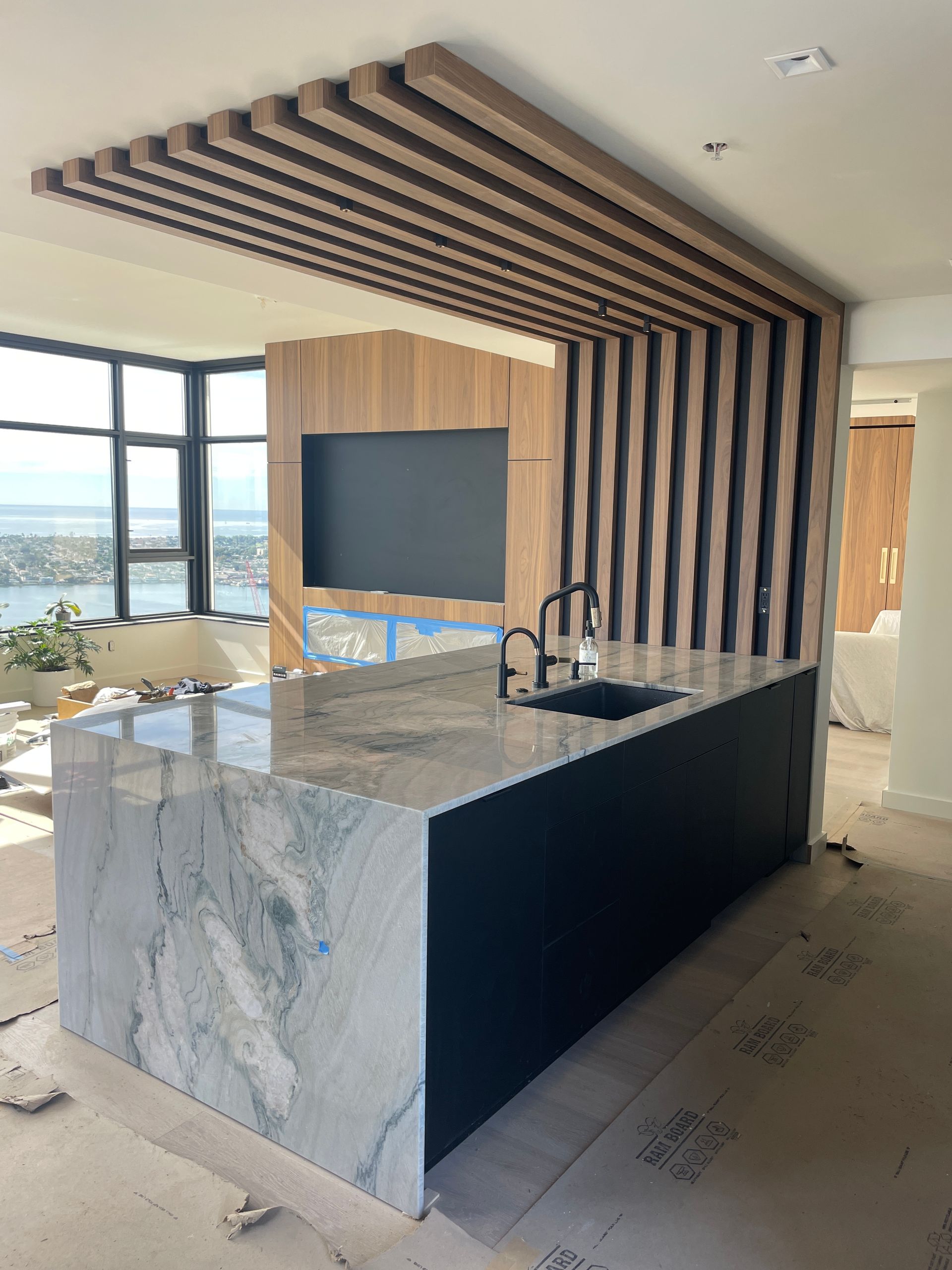 Modern kitchen with marble island, black cabinetry, wood slat ceiling, and ocean-view windows