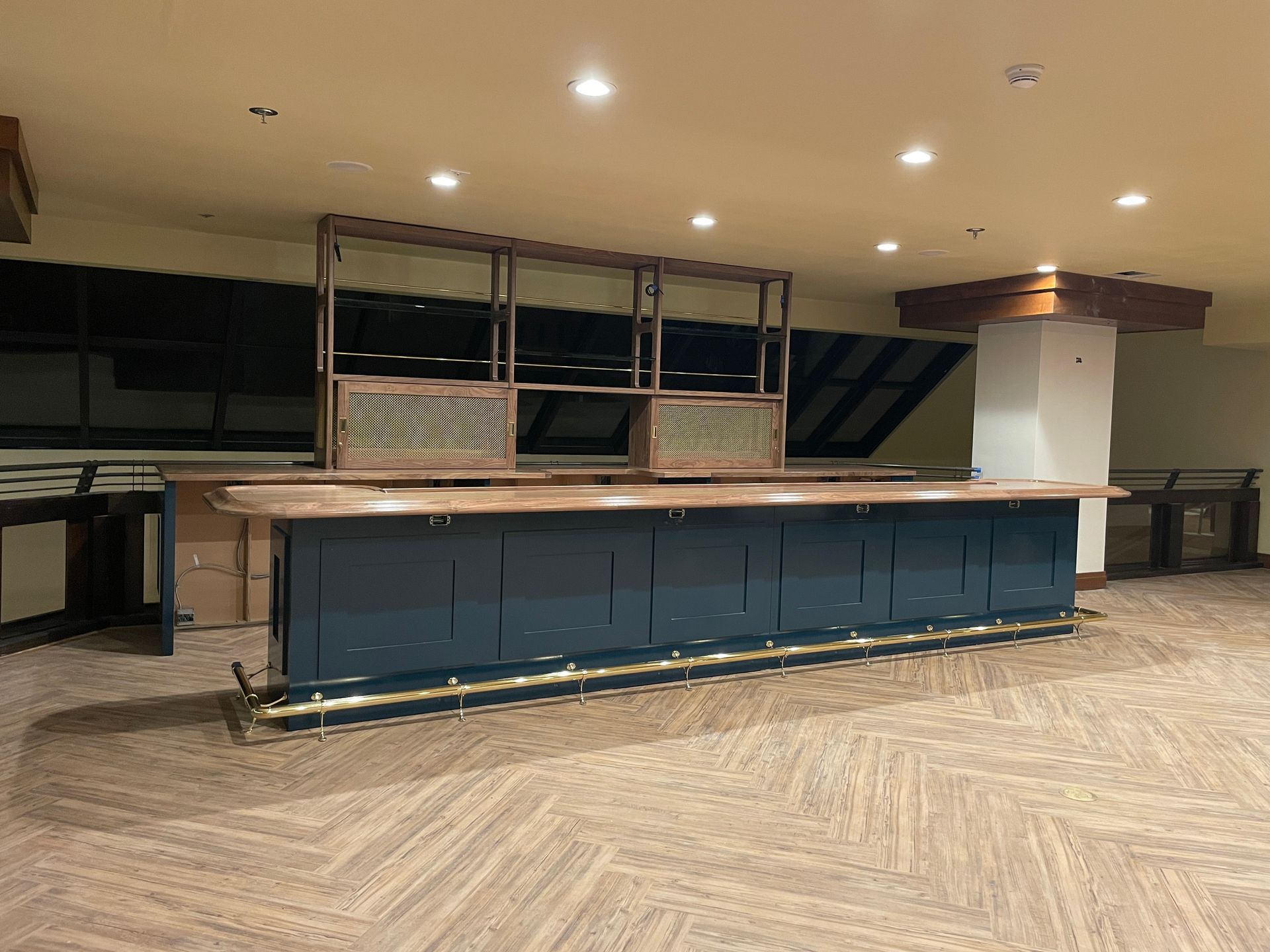 Empty hotel-style bar area with blue counter, wood floor, and recessed ceiling lights