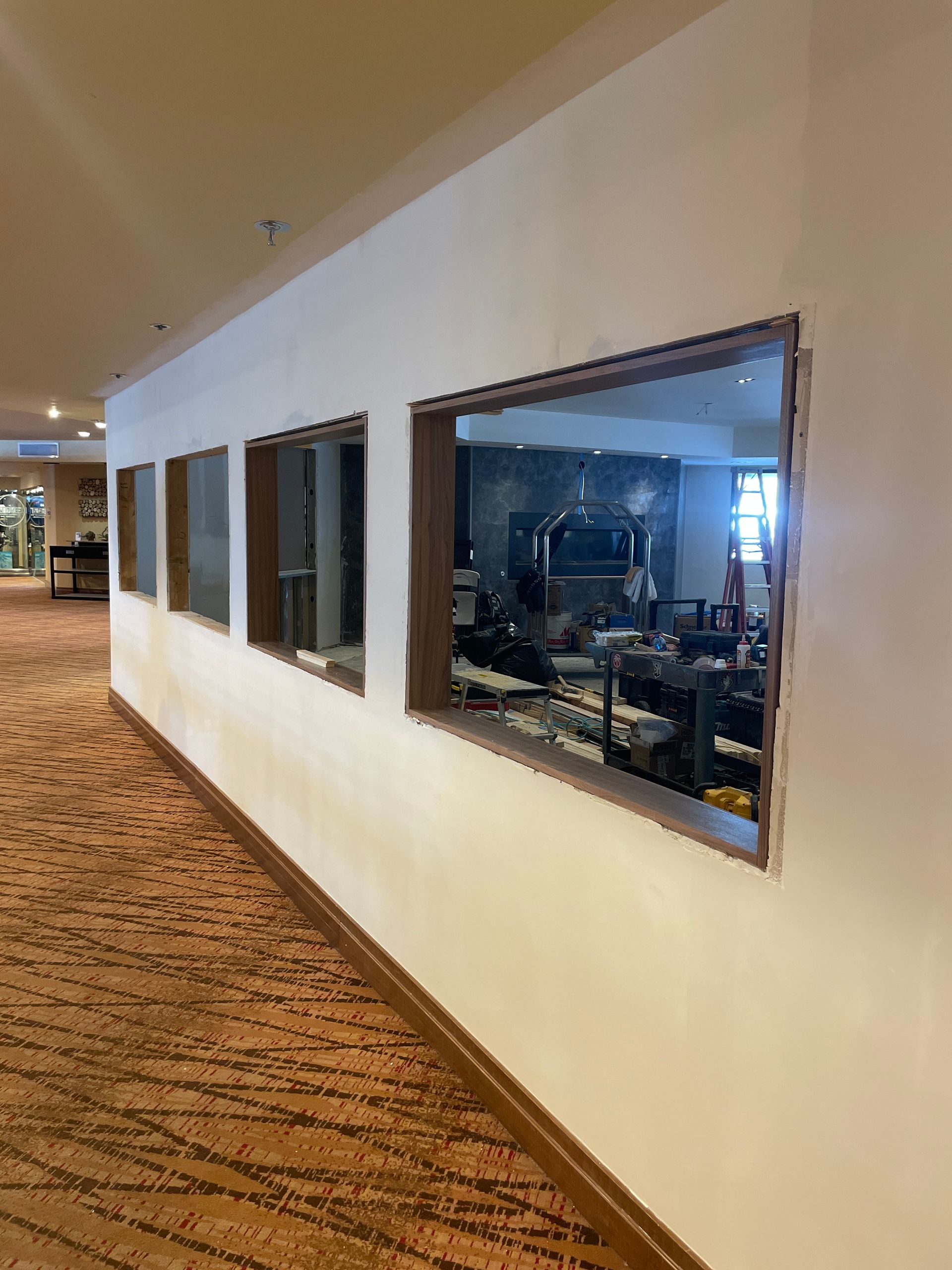 Hallway with large windows overlooking a dimly lit restaurant kitchen and seating area