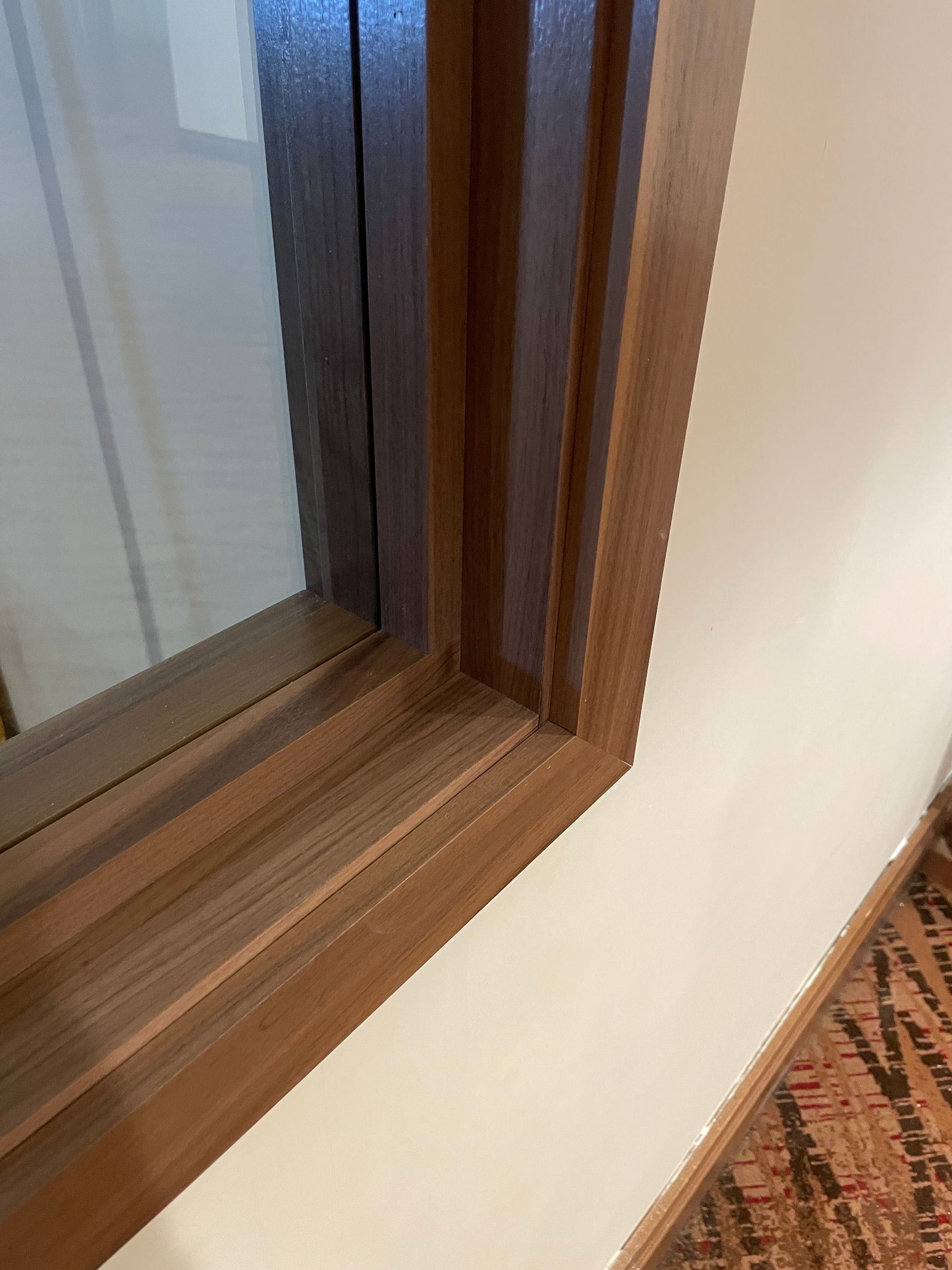Wood-framed window corner beside a cream wall and patterned carpet