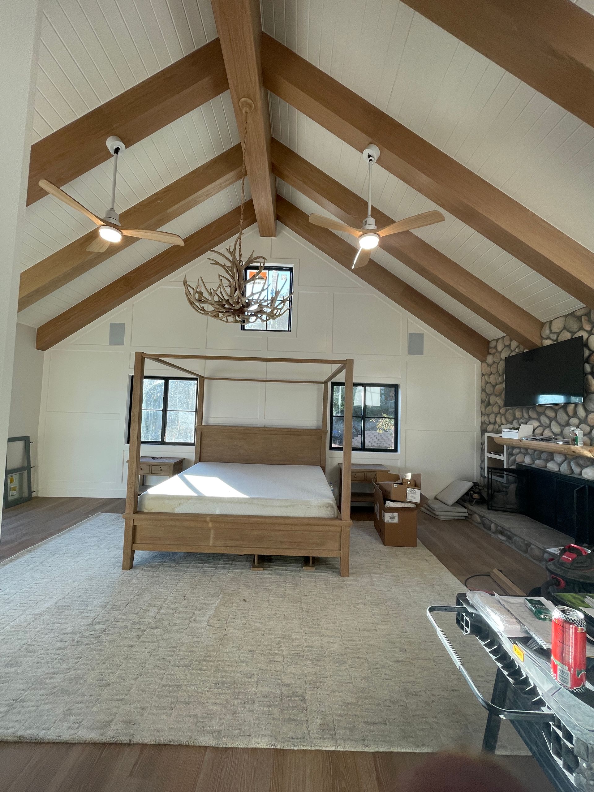 Spacious attic bedroom with wood beams, a canopy bed, carpet, ceiling fan, windows, and fireplace.