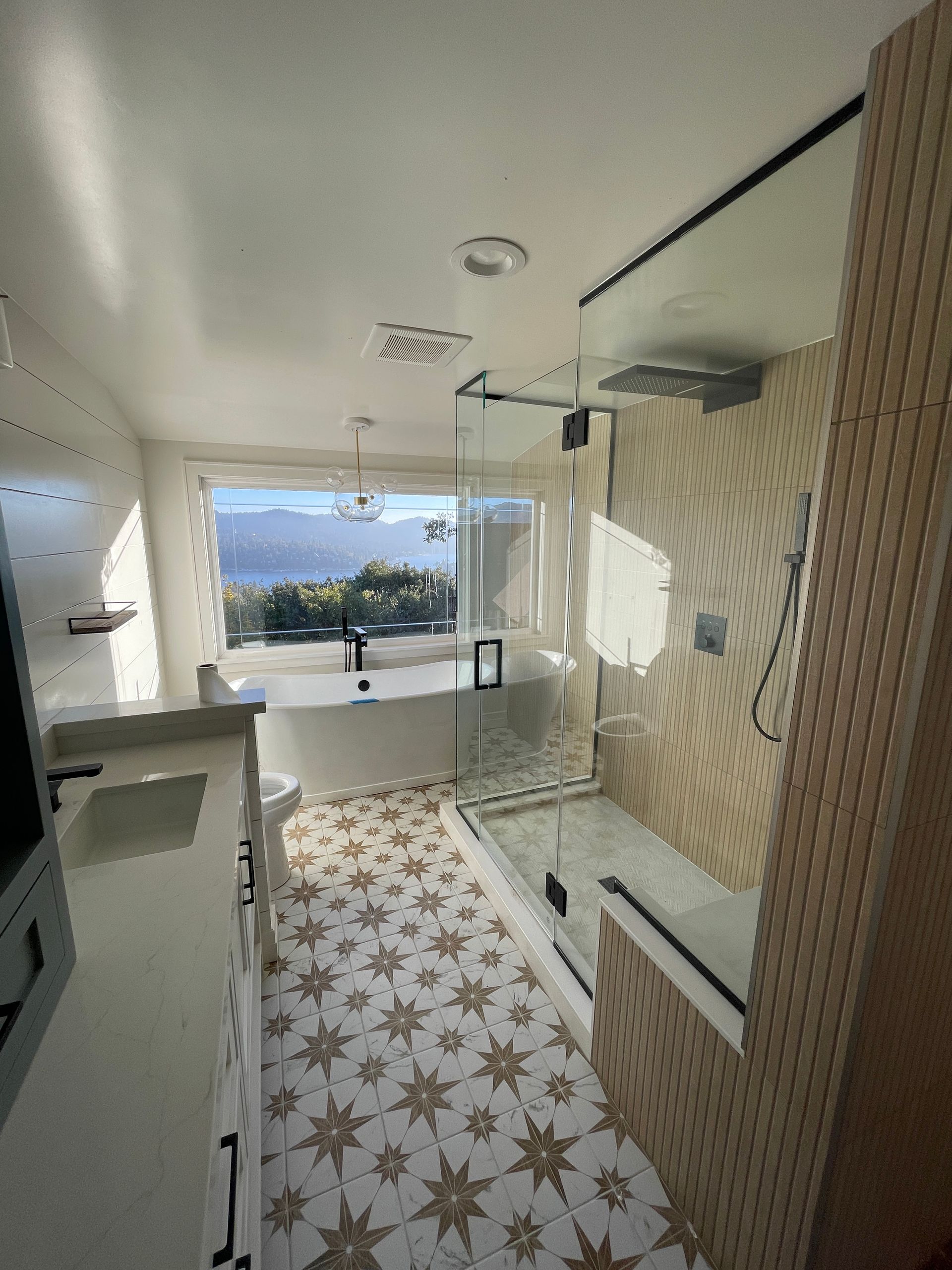 Bright tiled bathroom with a large window overlooking mountains and water.