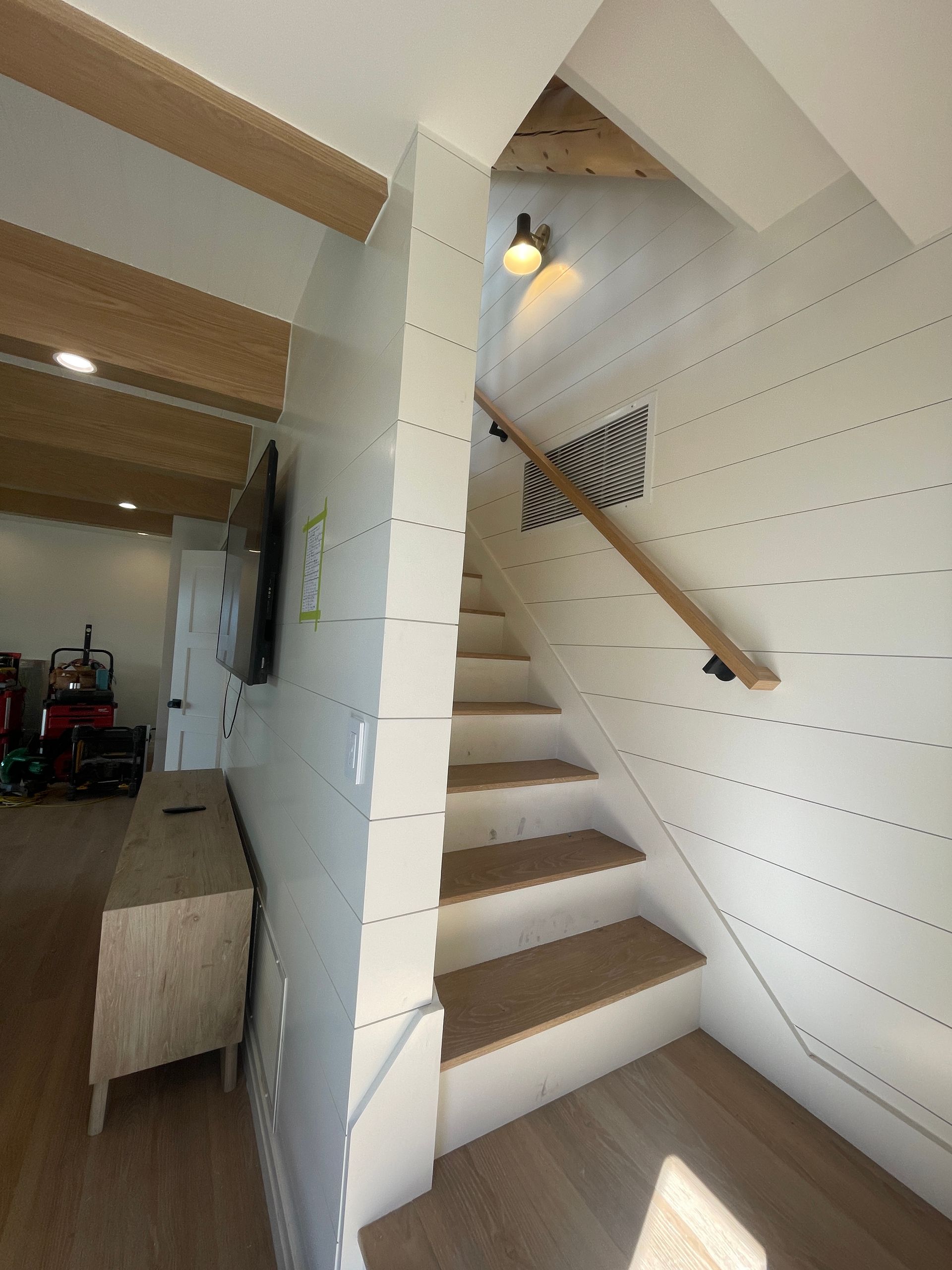 Bright stairway with white paneled walls, wooden steps, and a handrail in a loft-style interior.