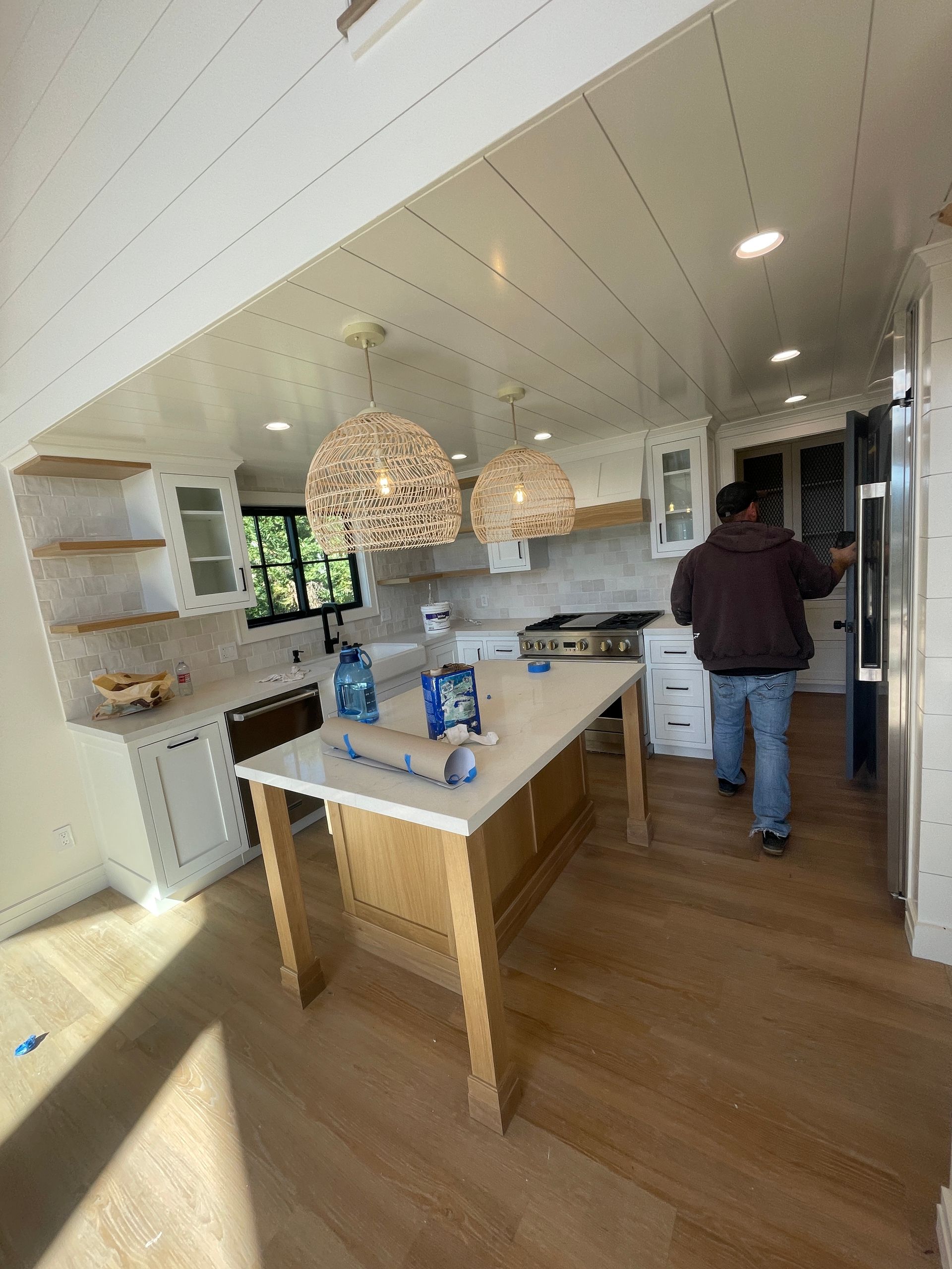 Bright, modern kitchen with a central island, pendant lights, and a person standing by the counter.