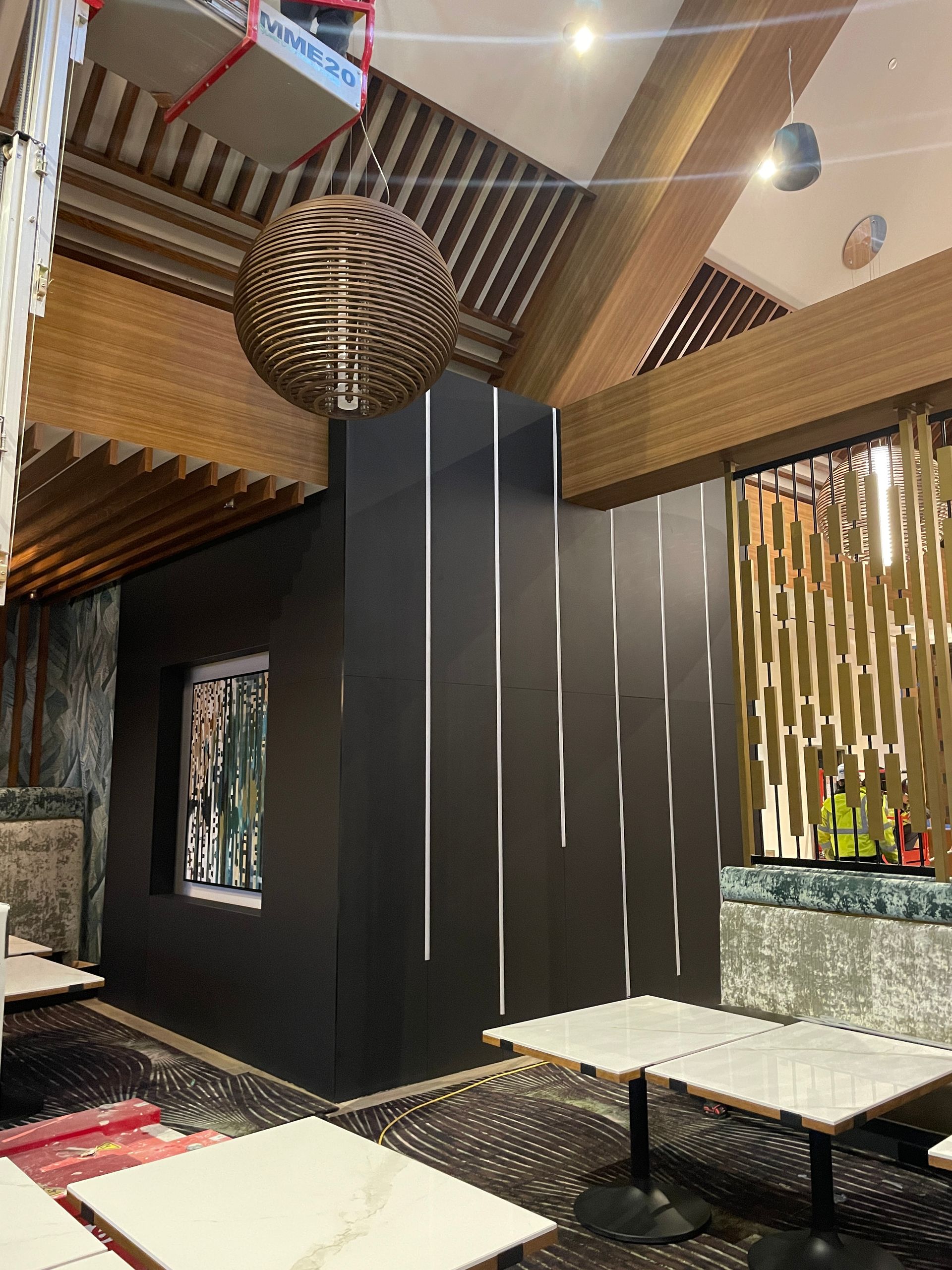 Modern restaurant interior with dark walls, striped wood ceiling, hanging globe lights, and mosaic tables