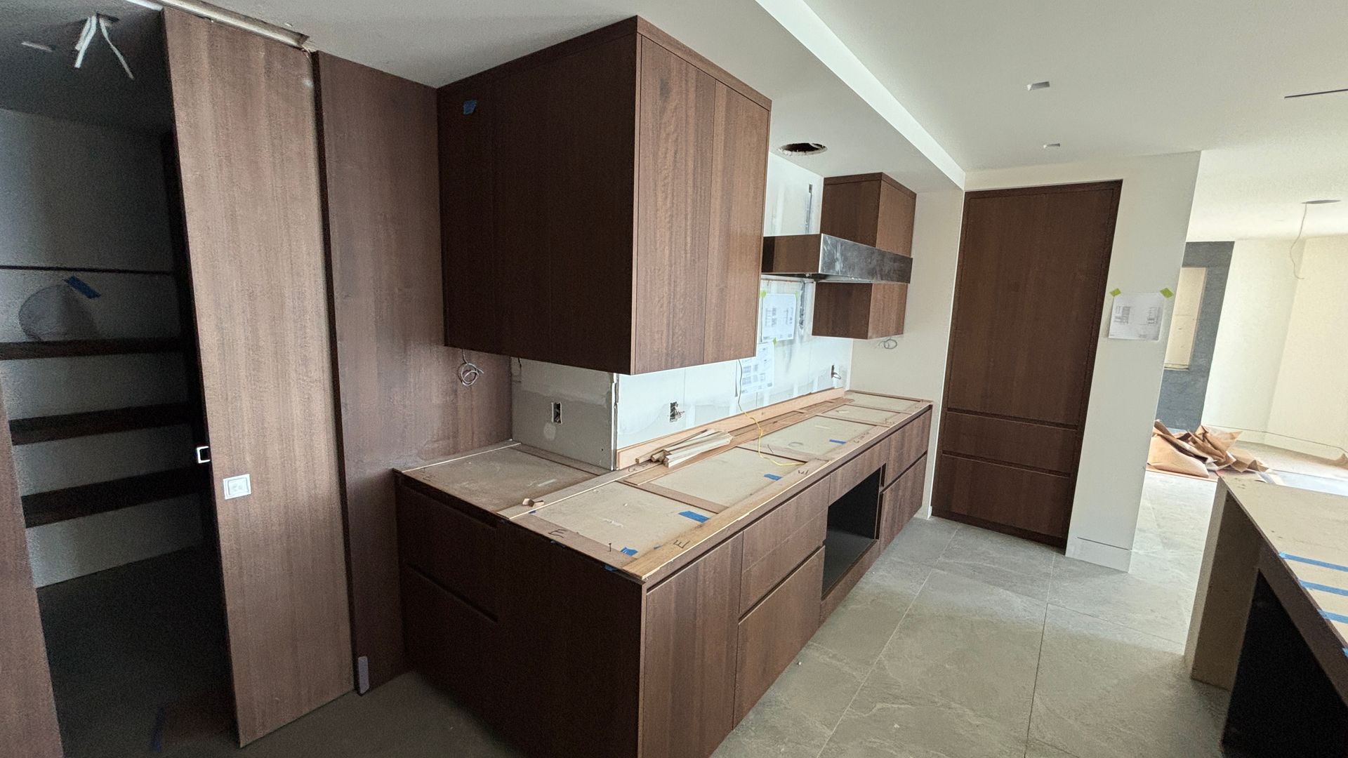 Modern kitchen with dark wood cabinets, white countertops, and an open doorway to another room.