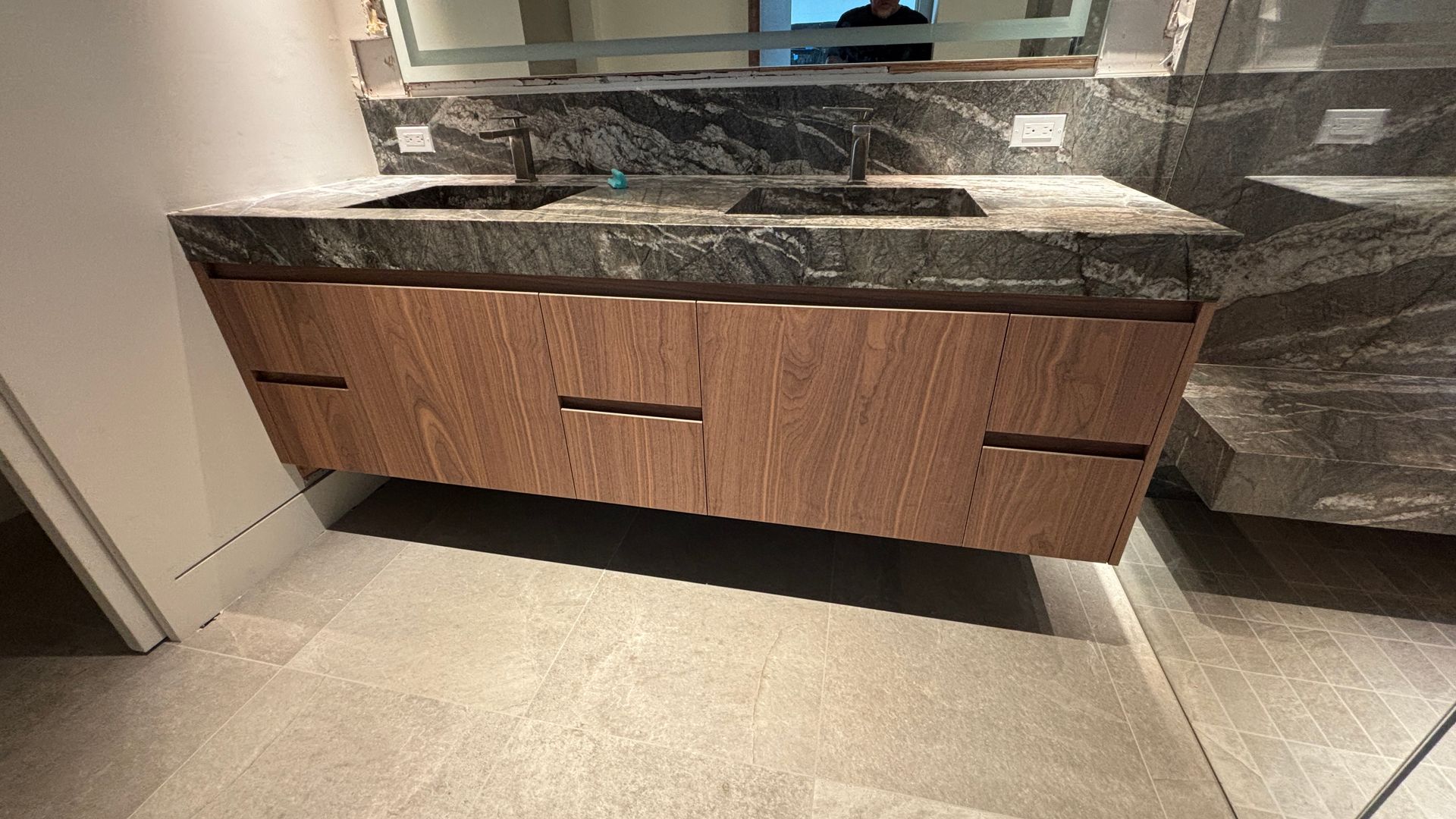 Modern bathroom vanity with dark granite countertop and wood drawers beneath a mirror.