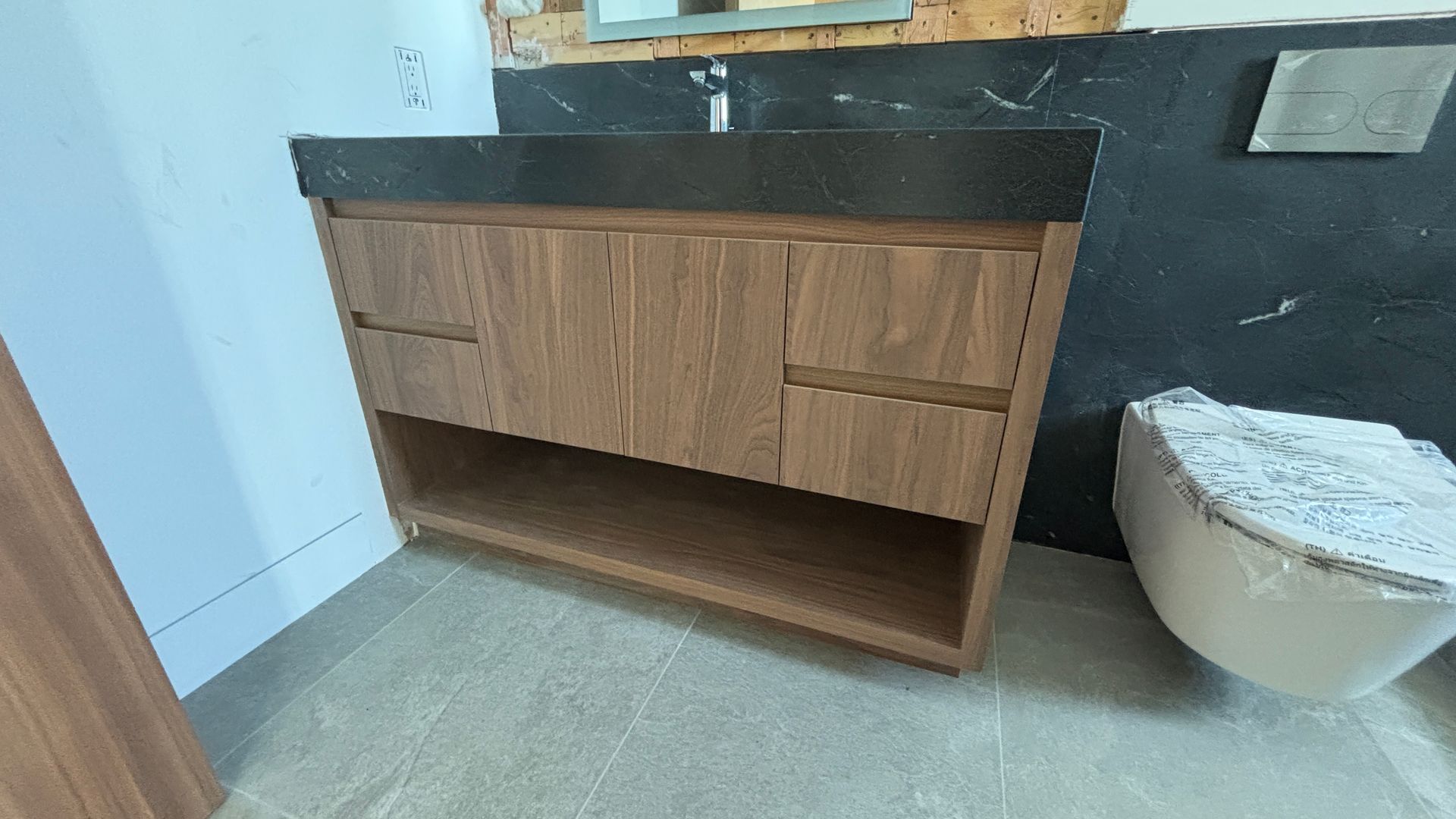 Bathroom vanity with wood drawers and open shelf, black countertop, and a toilet beside it