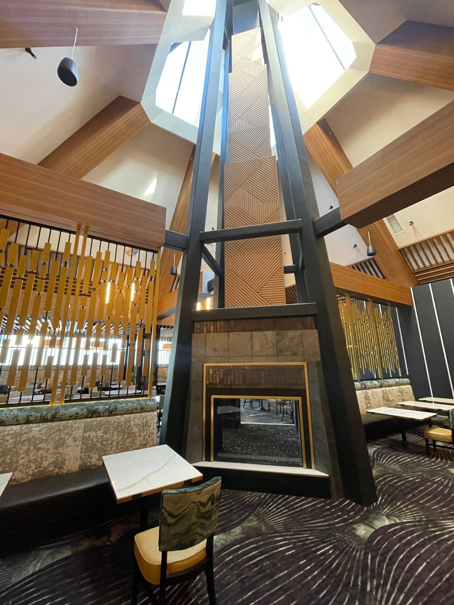 Modern lounge with a tall central fireplace, skylight, wood beams, and a single chair by the window.